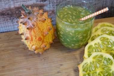 Boynuzlu kavun meyvesi, dilimlenmiş kiwano ve tahtanın üzerinde tohumlu bir bardak ferahlatıcı meyve suyu.