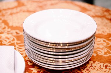 Zarif altın jantlı, el değmemiş beyaz yemek tabakları zarif bir turuncu masa örtüsünün üzerinde duruyor. Resmi bir etkinliğe ya da güzel bir yemek düzenine hazır..