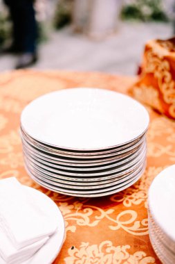 Dekoratif jantlı beyaz seramik tabaklar resmi bir etkinlik ya da büyük bir toplantı için hazırlanmış zarif turuncu bir masa örtüsünün üzerinde duruyor. Yemek, restoran ya da...