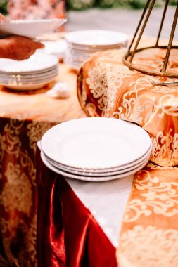 Temiz beyaz tabaklar zarif bir açık büfe masasına istiflenir. Lüks altın desenli masa örtüsüyle süslenir. Resmi bir etkinlikte ya da kutlamalarda misafirler için hazırdır..