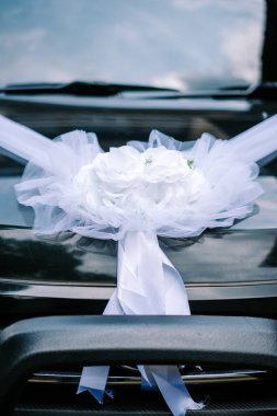 Büyük beyaz bir çiçek buketi ve akmakta olan kurdelelerle süslenmiş koyu renkli lüks bir arabanın yakın çekimi, özel bir düğün günü kutlaması için hazır..