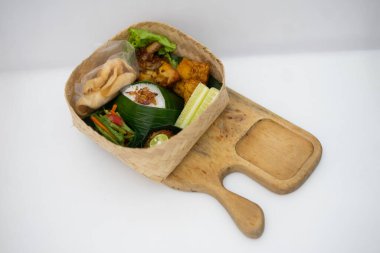 Otantik Endonezya mutfağı büyüleyici bir bambu sepetinde sunuluyor, kokulu pirinç, baharatlı tavuk, tempeh, taze sebze ve biber ezmesi, geleneksel bir yemek için mükemmel.
