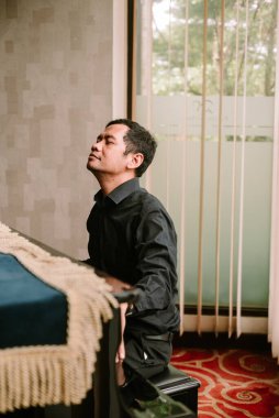 Koyu renk tişörtlü bir adam piyano çalar gözleri kapalı, tamamen güzel müziğe dalmış. İfadesi, melodiye karşı derin bir konsantrasyon ve tutku gösteriyor..