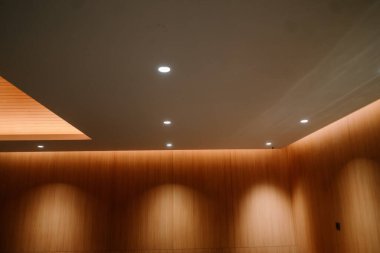 Çağdaş bir iç mekan, sıcak ahşap duvar panelleri ve çoklu spot ışıkları olan beyaz bir tavan, sofistike ve davetkar bir atmosfer yaratıyor..