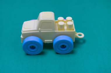 Canlı, açık sarı, mavi tekerlere çarpan plastik bir oyuncak kamyon pürüzsüz, sağlam bir deniz mavisi arkaplanına karşı duruyor. Çocukluk, oyun ve basitlik temaları için mükemmel..