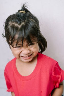 Sevimli bir çocuğun komik, neşeli bir yüz ifadesi sergileyen, gözlerini kısarak ve geniş bir gülümsemeyle yakın plan portresi. Saf neşe ve mutluluğu yakalar..