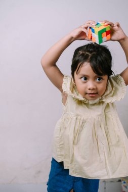 Neşeli genç bir kız kafasının üstünde ilginç bir ifadeyle renkli bir bulmaca küpü tutuyor. Bu neşeli an çocukluk sevincini, problem çözmeyi ve entelektüel gelişimi yakalar..