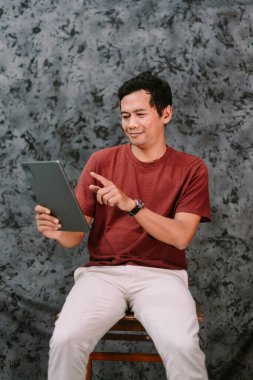 Kapalı alanda tablet kullanan Güneydoğu Asyalı bir adamın portresi. Modern teknoloji kavramı, çevrimiçi aktivite ve dijital eğlence.