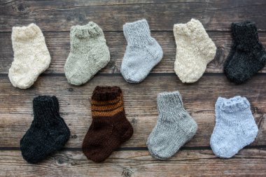 Koyu ahşap arka planda yün iplikten yapılmış küçük ve sıcak yeni doğan çoraplar.
