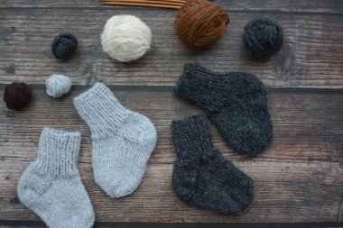 Koyu ahşap arka planda yün iplikten yapılmış küçük ve sıcak yeni doğan çoraplar.
