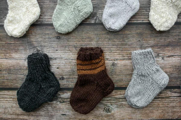 Koyu ahşap arka planda yün iplikten yapılmış küçük ve sıcak yeni doğan çoraplar.