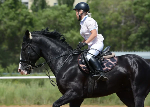 Mulher em um preto pulando cavalos em movimento — Fotografia de Stock