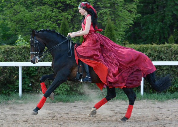 Женщина в красном платье на скачущей лошади

