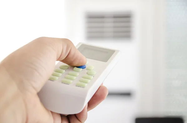 Main avec télécommande dirigée sur le climatiseur — Photo