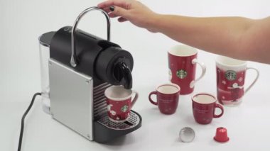Alüminyum kapsüller kullanarak otomatik Nespresso makinesinde mevsimlik Noel espresso yapmak. El Starbucks bardağını kahve makinesine koyar ve sıcak kahve yapar.