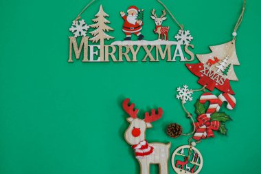 Bayramlık Noel süslemeleri düz yerde metin fotokopi alanı ile yatıyordu. Yeşil arka planda mevsimsel kompozisyon figürlerinin üst görünümü, Mutlu Xmas işareti ile.