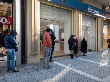 Selanik, Yunanistan - 18 Ocak 2021: Hükümetin COVID-19 tedbirlerini gevşetmesi sonrasında toptan mağazalar yeniden açıldı. Maskeli kalabalık, Coronavirus önlemleri ticareti etkilerken dükkanların dışındaki mesafesini koruyor..