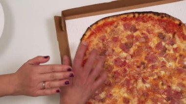 Kart kutusunun üstünde pizzayı döndürerek, bir dilim seçerek. Kadın eli onu aniden durdurup, beyaz bir tabakta pişmiş yemek servis ederken erkek eli kesiği yakalamaya çalışıyor..