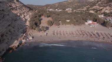 Akdeniz arazisi Yunan plajı kayalık insansız hava aracı tanımlanamayan banyolarla çekim yapıyor. Girit adasındaki Matala kireçtaşı mağaralarının hava günü manzarası. Şemsiyeli sakin deniz yatakları..