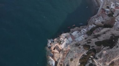 Deniz kenarındaki bir kayanın üzerine demirli caiques ile inşa edilmiş alçak binaların insansız hava aracı görüntüleri. Girit Adası 'ndaki sakin denizde sakin sularda yüzen balıkçı teknelerinin görüntüsü..