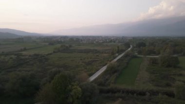 Yeşil ağaçların arkasında kırmızı kiremitleri olan küçük bir köy havası. Kuzey Yunanistan 'daki Kerkini bölgesinin akşam hava aracı görüntüsü, dağlık bir manzaraya sahip. 
