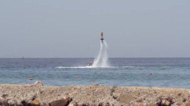 Su jetleriyle uçan sörf tahtası. Denizin üstünde kütük hortumu var. Sporcu, gökyüzü arka planına karşı hidroflighting cihazıyla kıyıya yakın dönen ekstrem spor havası uyguluyor..