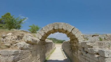 Olympia, Yunanistan 'ın antik spor oyunlarına ev sahipliği yapan arkeoloji sahasındaki POV' u. Klasik zamanlarda mavi gökyüzüne karşı atletizm müsabakaları için taş kemer ve girişi inşa edildi..