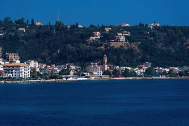 Zakynthos, Yunanistan 'ın deniz kenarındaki alçak binaları ile adanın başkenti. Ortodoks kilisesinin çevresindeki kırmızı fayanslı evler, sakin deniz ve yeşil ağaçlı tepe..