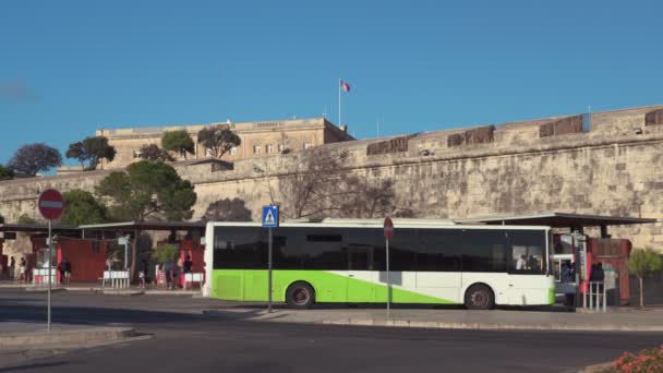 バレッタ マルタ公共交通機関バスターミナルに駐車 市壁の隣のバレッタ中央バス停の緑と白のディーゼルコーチ 晴れた日に — ストック動画