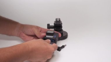 GoPro Kahraman 10 mavi logolu siyah. Eller akü ve aksesuarlarla kamerayı beyaz arkaplan üzerine monte ediyor.. 