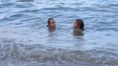 Küçük üçüz kız kardeşler okyanus sahilinde dalgalarda yüzerler. Yüksek kalite 4k görüntü