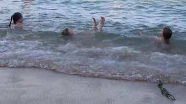 Küçük üçüz kız kardeşler okyanus sahilinde dalgalarda yüzerler. Yüksek kalite 4k görüntü