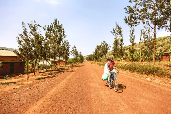 The man carrying stuffs with bicycle on the plain red earth road without bulges. — Stockfoto