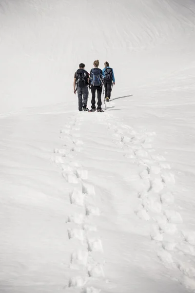 Three people walking away with snowshoes — Stock Photo, Image