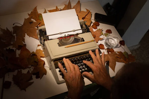 Top view of man\'s hands on a typewriter with autumn leaves , inspired writer