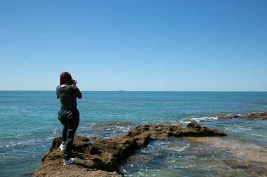 Sırtüstü yatmış elinde kamerayla kayalıklara bakan bir kadın.