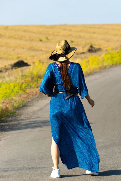 Vrouw in blauwe jurk en hoed lopen op de weg — Stockfoto