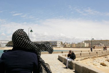 Özgür bir kadın, Cadiz bölgesinde başı örtülü olarak deniz kenarında yürüyor.-