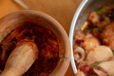 Eldivenli kadın elleri soslu kalamar pişiriyor, karides kafası eziyor.