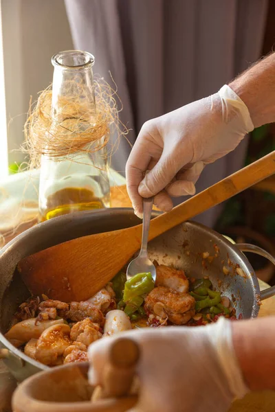 Mujeres manos con guantes cocinando calamares en salsa, aplastando cabezas de gambas Imagen De Stock