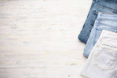 Ahşap arka planda üst üste dizilmiş kot pantolonlar, düz yatış. Uzak metni yerleştir.