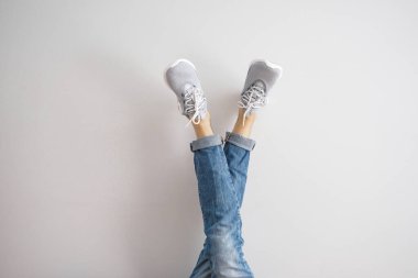 Gri arka planda kot ve spor ayakkabı giyen genç bir adamın bacakları..