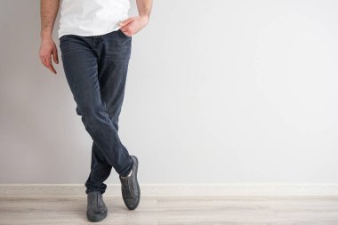 Gri arka planda kot ve spor ayakkabı giyen genç bir adamın bacakları..