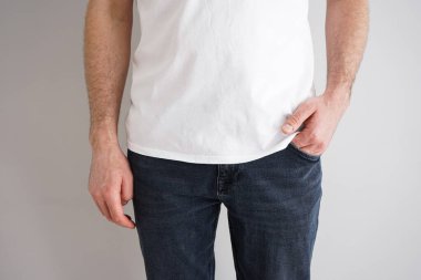 Gri arka planda eli cebinde kot giyen genç bir adamın bacakları..