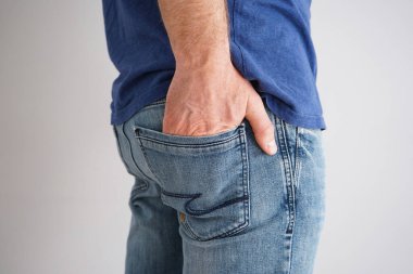 Gri arka planda eli cebinde kot giyen genç bir adamın bacakları..