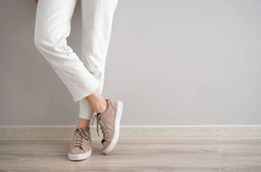 Gri arka planda kot pantolon ve spor ayakkabı giyen genç bir kızın bacakları..
