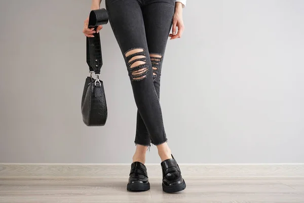 一个穿着黑色牛仔裤 头戴灰色背景的袋子和鞋子的小女孩的腿 — 图库照片