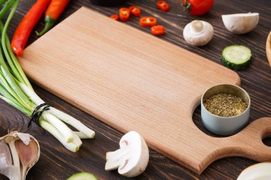 Ahşap kesim tahtası ve ahşap masa arkasında pişirmek için taze malzemeler, yakın plan.