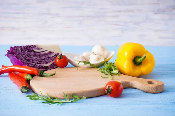 Wooden cutting board and vegetables on wooden background, place for text.