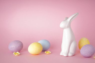 Paskalya tavşanı ve pembe arka planda renkli paskalya yumurtaları. Mesaj için yer. Mutlu Paskalyalar.